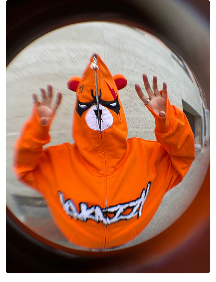 Wearing a Seakoff Furious Orange Bear Hoodie with red embroidery and an Angry Bear design, a person holds their hands up. The hoodie, made from premium 400GSM cotton, is captured in a fisheye effect.