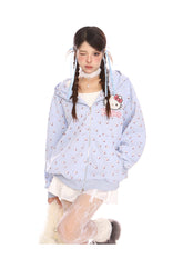 A person with long braided hair is wearing a Hello Kitty Pink Kawaii Hoodie from Seakoff, featuring a cute oversized zip-up with cat ear hood and all-over print. They pair it with a white dress and patterned tights, winking and tilting their head slightly to embrace the kawaii style.