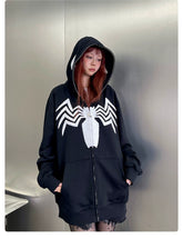 With long hair and confidence against a metallic wall, someone sports the Seakoff Venom Spider Hoodie—an oversized black and white zip-up sweatshirt. Perfect for streetwear fans, it features a bold white spider emblem on its 400GSM fabric.