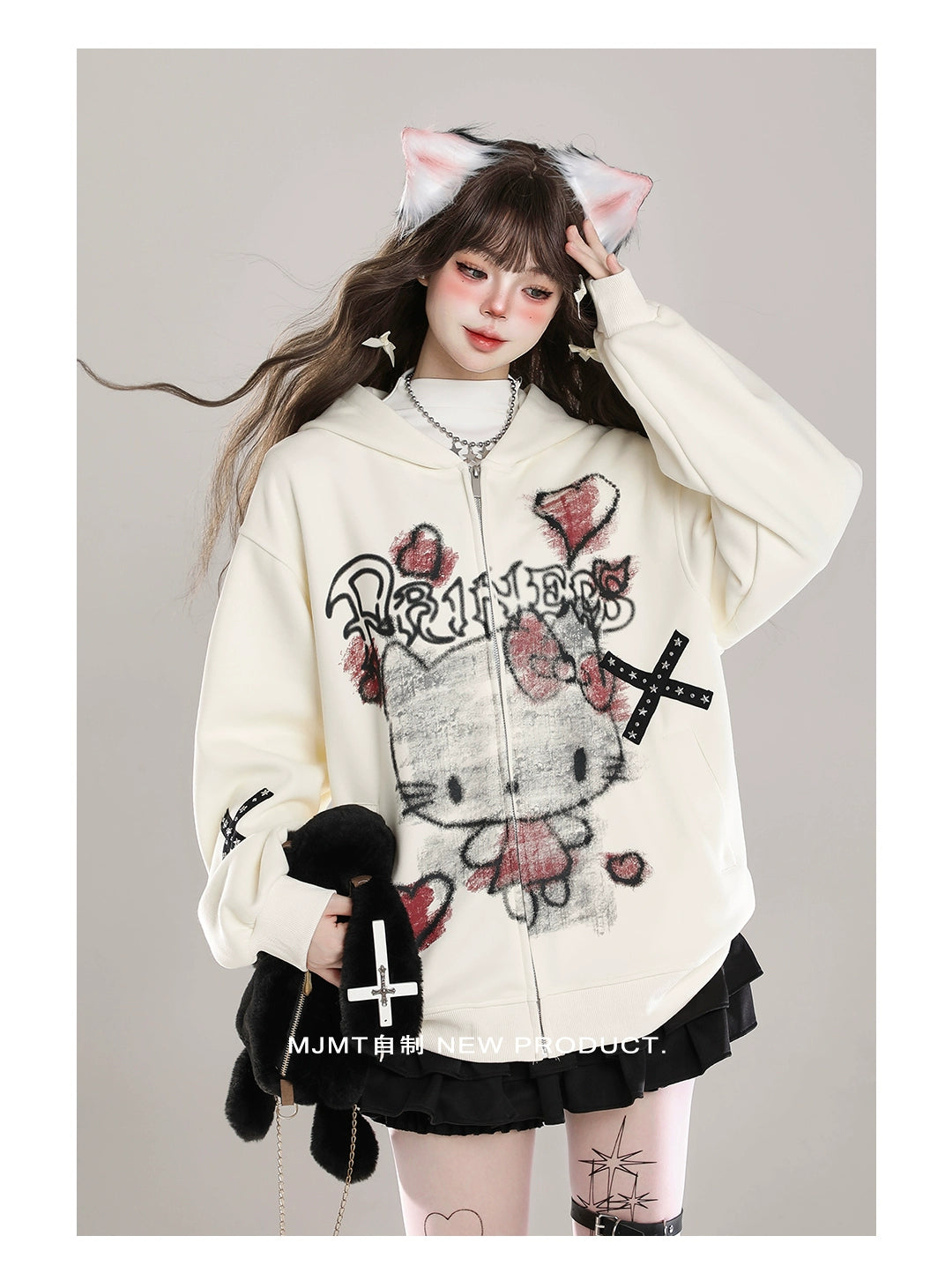 A person wears a cream-colored Seakoff Gothic Hello Kitty Princess Hoodie featuring edgy heart and cross graphics. Paired with a short black skirt, knee-high socks, cat ear headband, long brown hair, and holding a black plush toy, they create an adorable alternative kawaii fashion look.