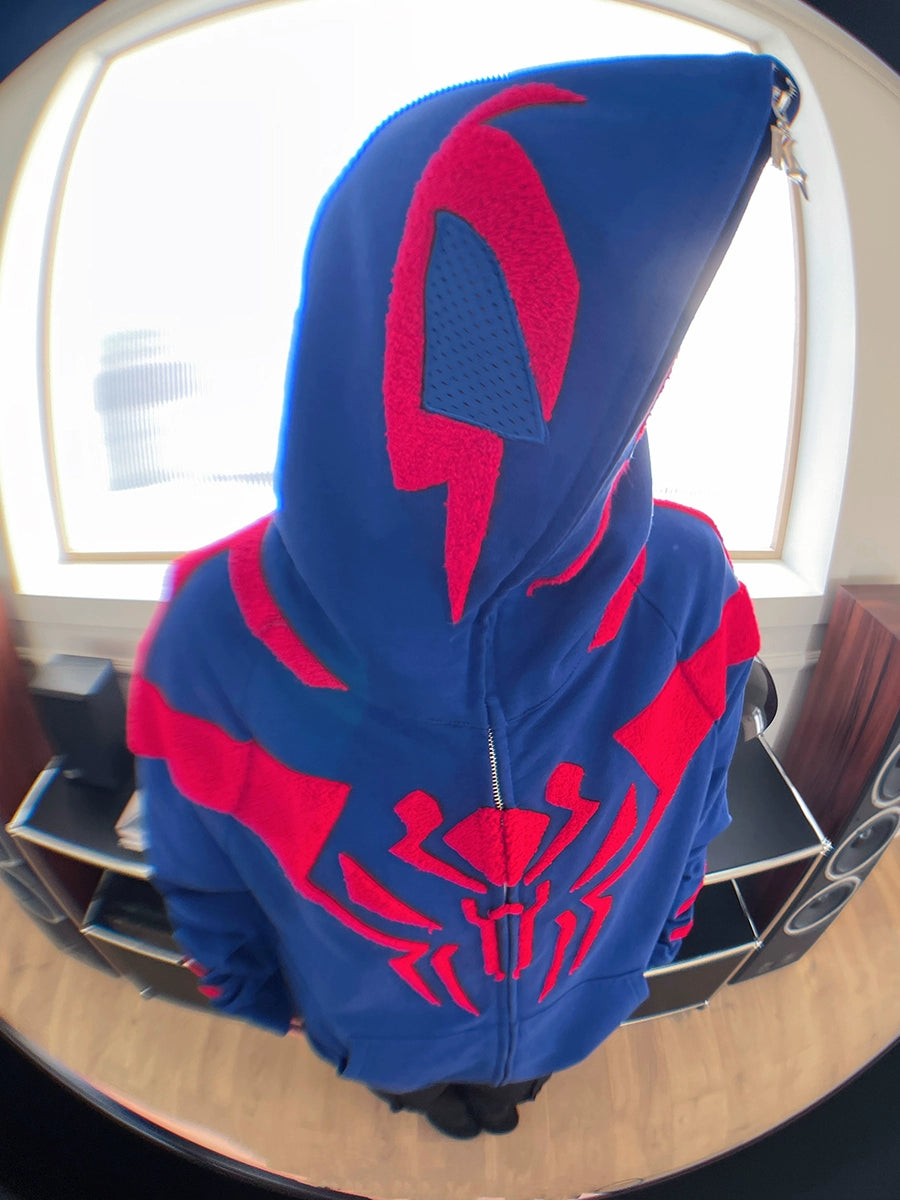 A person stands indoors by a window, face obscured, wearing the Seakoff Superhero Spider Hoodie—an oversized 400GSM blue and red zip-up sweatshirt for fans.