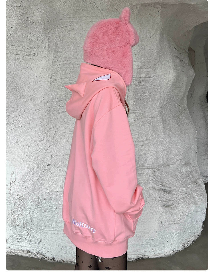 A person faces sideways, donning a pink, Batman-inspired hoodie with cat ears and black star-patterned tights against a textured light wall. The oversized Seakoff hoodie has "Hukzzang" embroidered near the hem—a unique find for superhero enthusiasts.