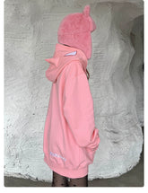 A person faces sideways, donning a pink, Batman-inspired hoodie with cat ears and black star-patterned tights against a textured light wall. The oversized Seakoff hoodie has "Hukzzang" embroidered near the hem—a unique find for superhero enthusiasts.