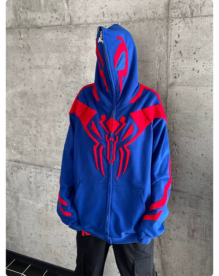 A person in a Seakoff Superhero Spider Hoodie, featuring red and blue spider and web patterns, stands against a gray concrete wall. The hood obscures their face as they rest their hands in the sweatshirt&