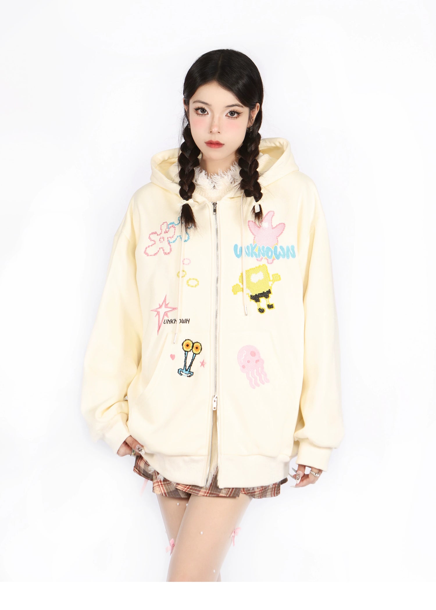 Wearing a Kawaii Pastel Cartoon Hoodie by Seakoff, featuring playful embroidered designs like a jellyfish and robot, a person with braided hair poses seriously in plaid skirt and stockings on a white backdrop.