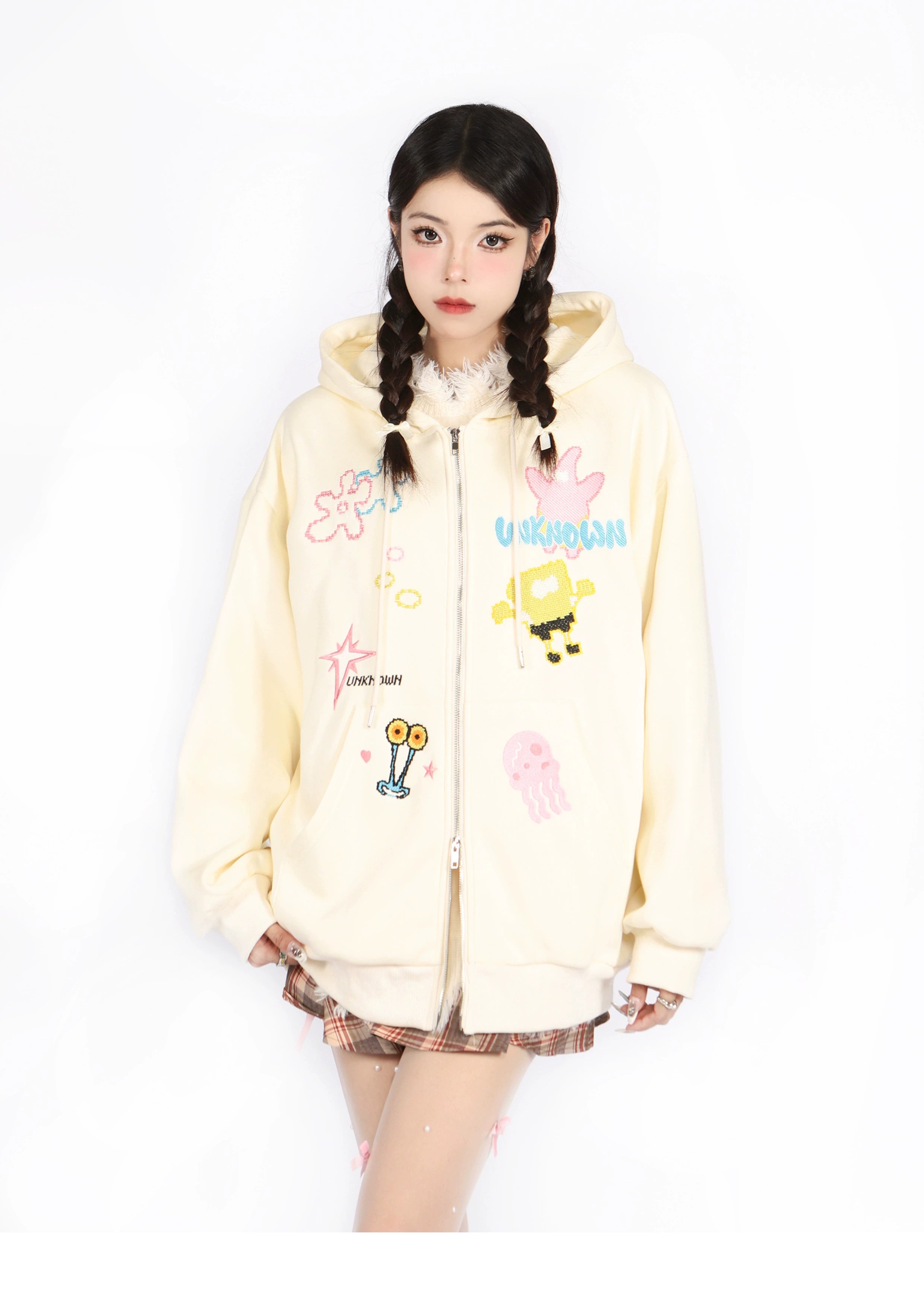 Wearing a Kawaii Pastel Cartoon Hoodie by Seakoff, featuring playful embroidered designs like a jellyfish and robot, a person with braided hair poses seriously in plaid skirt and stockings on a white backdrop.