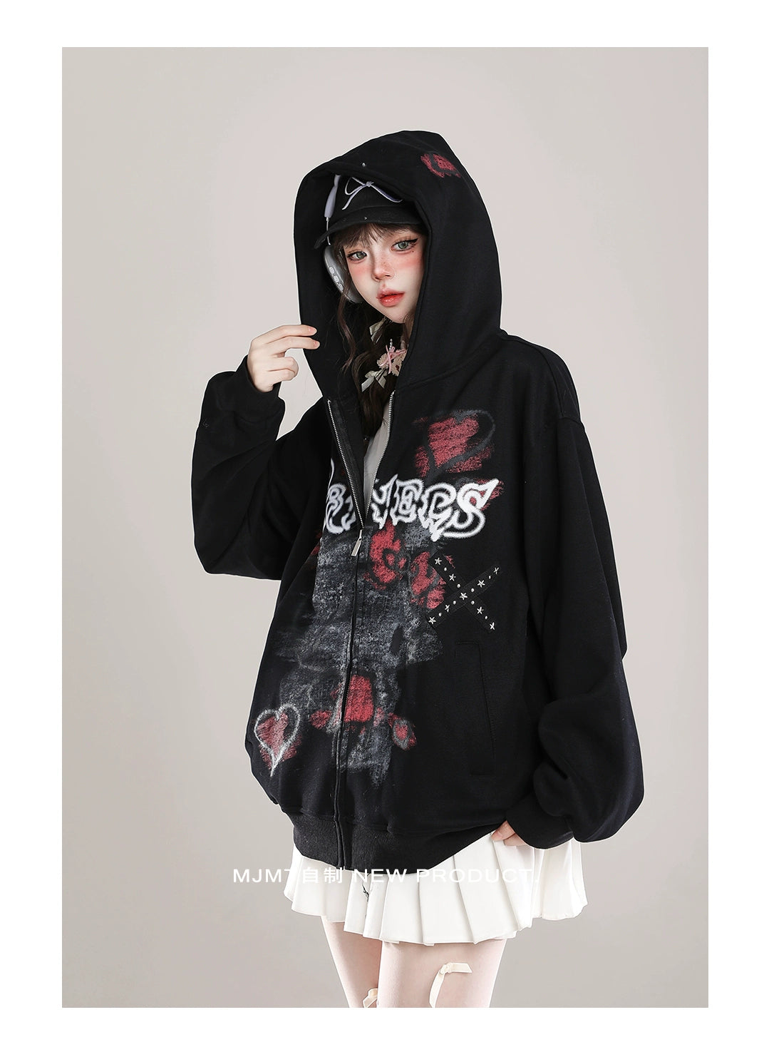 A person wears the Gothic Hello Kitty Princess Hoodie by Seakoff, featuring edgy heart and cross graphics on a black background with the text "LOVERS." They accessorize with a black cap and white skirt, effortlessly blending alternative fashion elements.