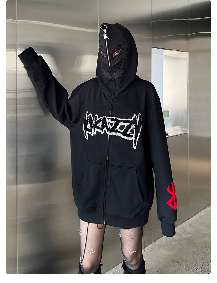 A person wears the Berserk-Inspired Griffith Dark Knight Hoodie—400GSM black zip-up with a bold front design and red sleeve symbol. They have a black mask with eye details, standing in a metallic, reflective room with one arm extended.
