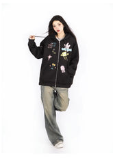 A person with long dark hair poses in a Seakoff Kawaii Pastel Cartoon Hoodie—featuring playful embroidered designs like jellyfish and spaceships. They embrace anime fashion with baggy jeans, white sneakers, and stand on one leg against a white background.