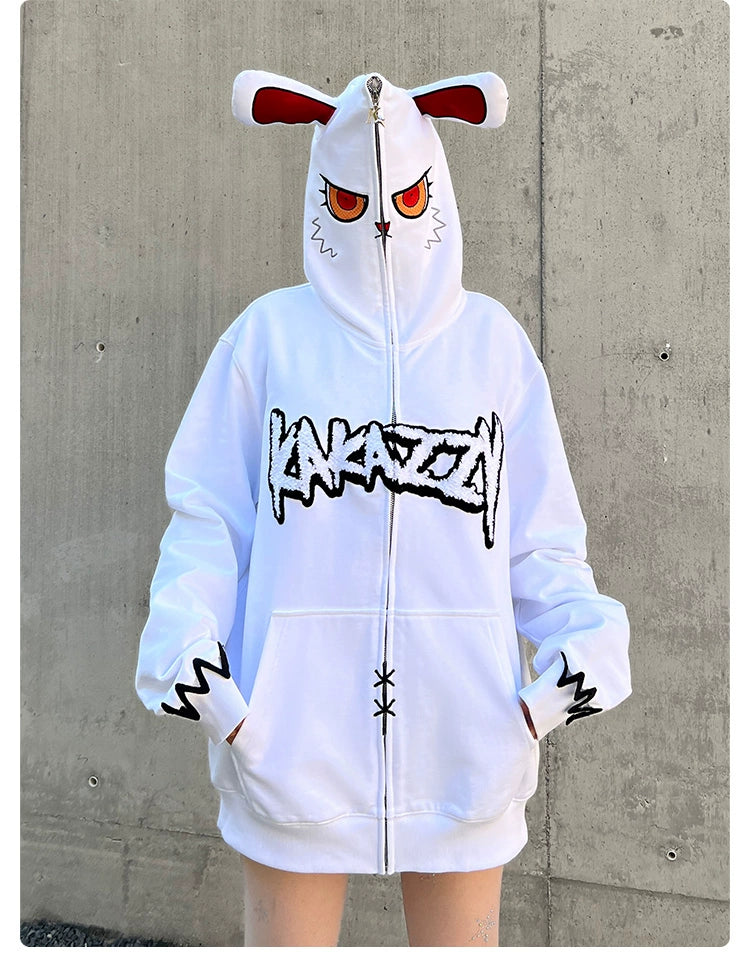A person sports the oversized Seakoff Fierce Bunny Hoodie, featuring a bunny ear design with red eyes and "KANAZAWA" across the chest. Claw motifs adorn the sleeves, standing out against a stark concrete wall.