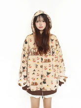 A person wearing the Seakoff MKCH Dog Print Hoodie, an adorable full-zip hoodie featuring a playful puppy pattern and "MUNCH." The beige hoodie with brown cuffs beautifully contrasts their long hair against a plain white background.