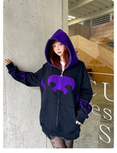 A person stands indoors near a concrete wall, wearing a striking Seakoff Dark Hero Hoodie—an oversized black and purple superhero zip-up sweatshirt with large patterns. The hood is up, long hair cascading out, and star-patterned leggings complete their streetwear vibe.