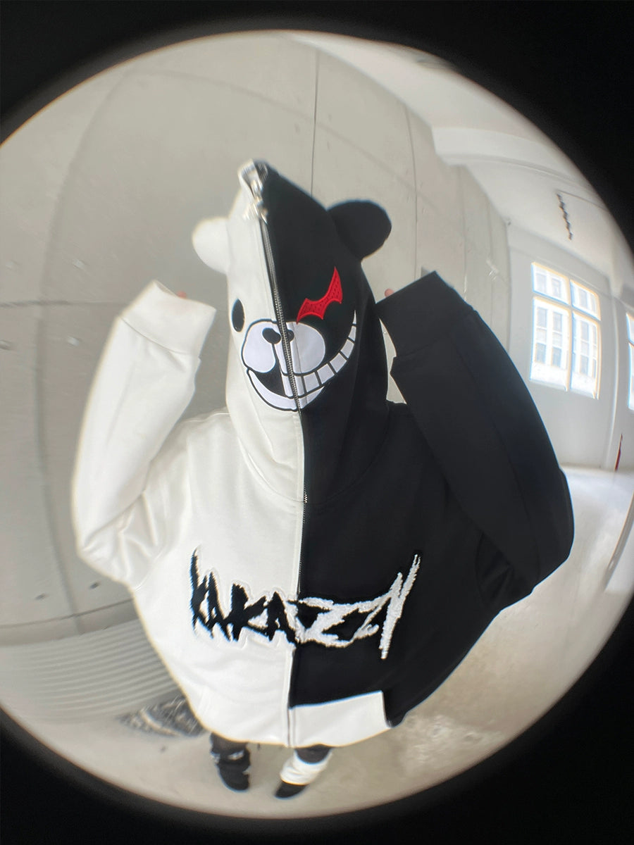 A Danganronpa fan wears a Seakoff Monokuma-Inspired Hoodie—an oversized black and white zip-up sweatshirt with a bear face and "MAD" text. Photographed with a fisheye lens, it shows circular distortion in the plain white room with windows.