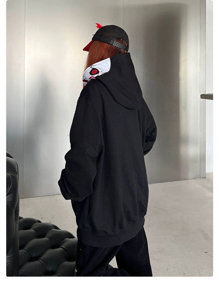 A person stands with their back to the camera, wearing a Seakoff Saw-Inspired Hoodie and a black cap with a red brim, in a room featuring a black sofa and metallic wall—an ideal setting for horror movie fans.
