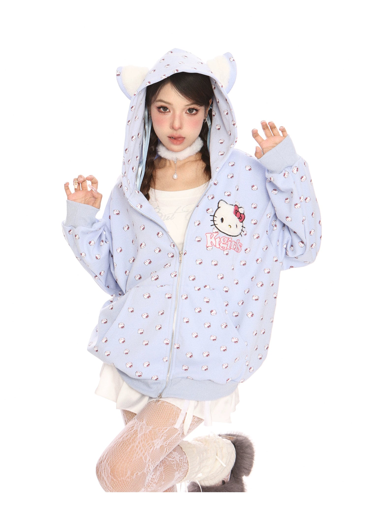 A person strikes a playful pose in a Hello Kitty Pink Kawaii Hoodie by Seakoff, featuring cat ears and an all-over print. They pair it with white lace stockings, fluffy shoes, and a choker, capturing kawaii fashion against a crisp white background.