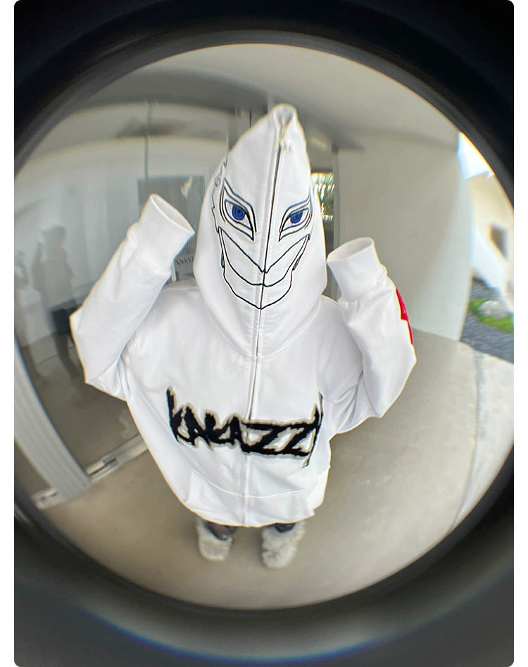 A person wears a Berserk Griffith-Inspired Hoodie, a white oversized zip-up sweatshirt with a face graphic on the hood and "KRAZZY" on the torso. Captured through a fisheye lens, the image distorts its surroundings—a style any Berserk fan would appreciate.