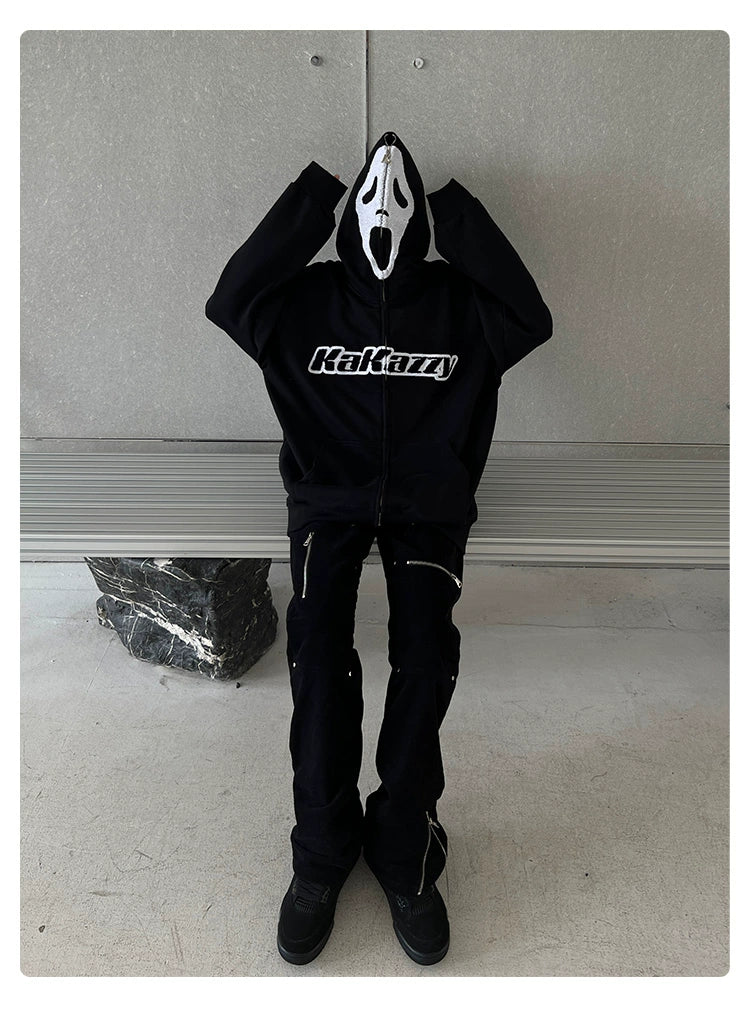 A person in a Seakoff Scream-Inspired Hoodie, a 400GSM oversized black zip-up horror movie sweatshirt, sits on a bench. They&