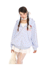 A person with long braided hair wears a Seakoff Hello Kitty Pink Kawaii Hoodie, an oversized zip-up with cat ear hood and all-over print, over a white layered skirt and lace stockings. Against a plain white backdrop, they exude kawaii fashion charm.