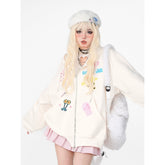 A long-haired blonde embodies kawaii fashion in a Seakoff Kelly Kitty Pastel Kawaii Hoodie, with adorable embroidered characters, a choker, and a pink pleated skirt. A fluffy white bag hangs over one shoulder as they pose against a plain background.