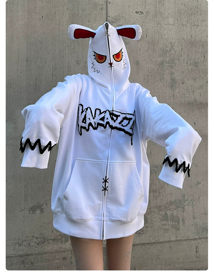 A person is wearing an oversized Seakoff Fierce Bunny Hoodie in 400GSM cotton, featuring a large cartoon face and long sleeves. The hood has playful bunny ears with bold "Kaka" print. A plain concrete wall backdrop highlights the unique style of the hoodie with red eyes.