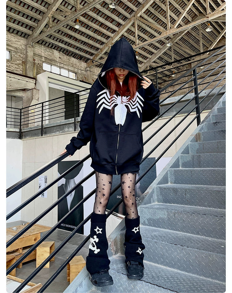A person in a Seakoff Venom Spider Hoodie, an oversized 400GSM black and white zip-up sweatshirt for superhero fans, stands on metal stairs. Their red hair contrasts with star-patterned tights and leg warmers, turning heads among streetwear enthusiasts amid metal railings and high ceilings.