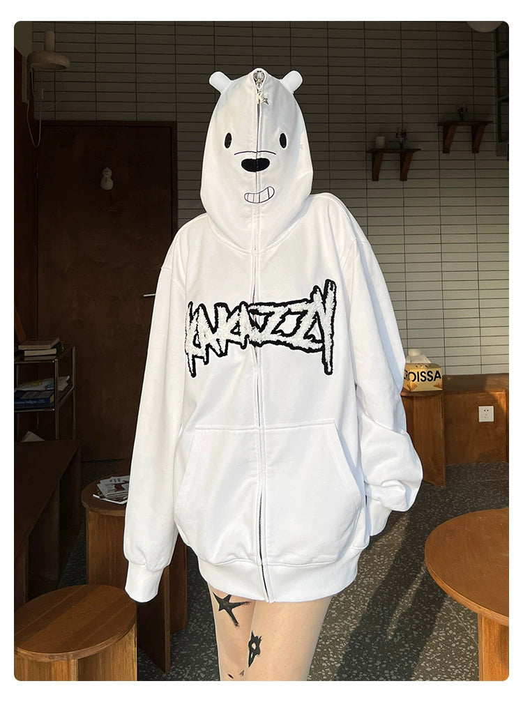 A person is flaunting a Seakoff Cute White Bear Hoodie, a 400GSM polar bear design featuring black embroidery, in a cozy room with tile walls and wooden furniture warmly lit by natural light.