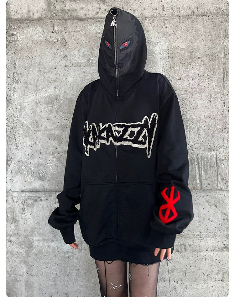 A person stands against a concrete wall wearing the Berserk-Inspired Griffith Dark Knight Hoodie, a black 400GSM zip-up oversized streetwear from Berserk. The hoodie features a graphic design on the front, a red symbol on the sleeve, and a hood up partially covering their face. They also wear sheer black tights.
