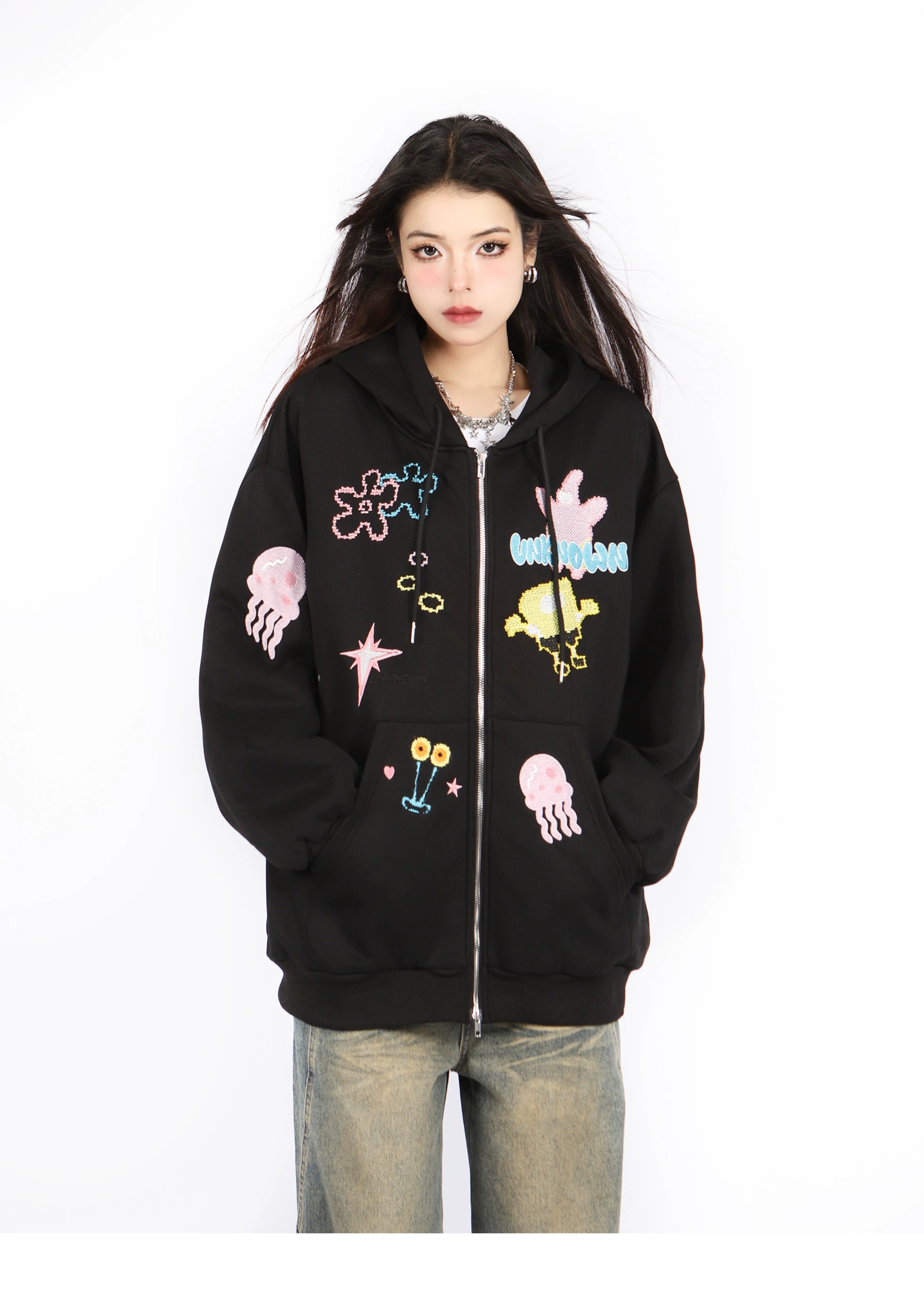 A person with long dark hair is wearing a Seakoff Kawaii Pastel Cartoon Hoodie, featuring playful embroidered designs like jellyfish and stars, along with light brown jeans, set against a plain white background.