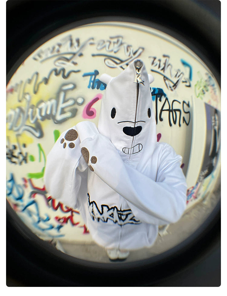 A person in a Seakoff Cute White Bear Hoodie, featuring a 400GSM polar bear design with ears and black embroidery, stands with arms crossed. The vibrant graffiti background is captured with a fisheye lens effect.