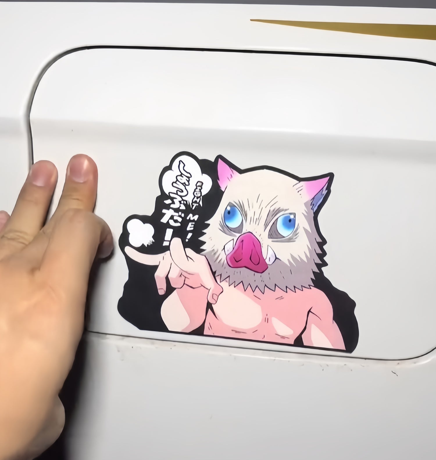 A hand is reaching to open a white car fuel door, which has a colorful sticker on it. The sticker depicts a muscular, anthropomorphic pig with blue eyes, speaking in stylized text with some Japanese characters.