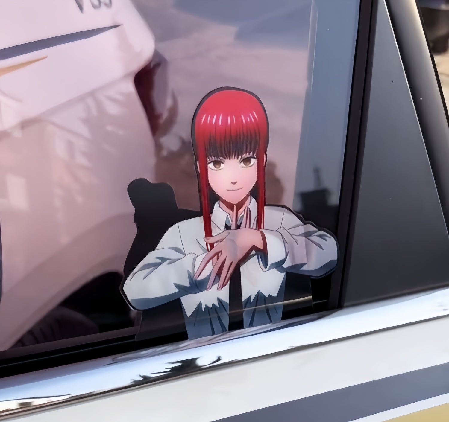 A car window features a sticker of an animated character with long red hair and a light-colored shirt. The character is positioned with hands in a gesture, against the backdrop of the vehicle's exterior.