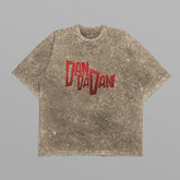 The Dandadan Oversized T-Shirt features a minimalist "Dan Da Dan" logo in bold red on the front, set against a speckled gray fabric with an Okarun side profile on the back, laid flat on a light gray background.
