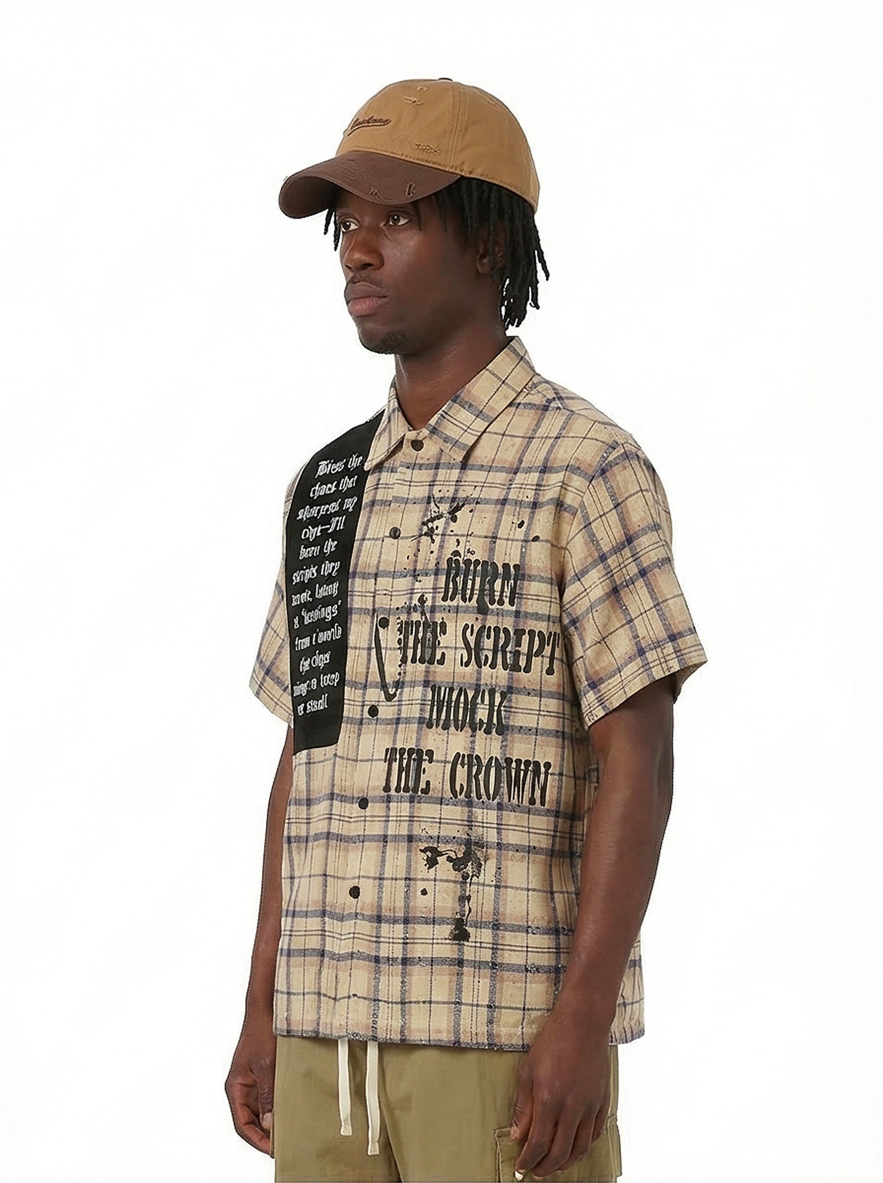 Man wearing tan plaid short-sleeve shirt with black Burn The Script graphic and brown cap