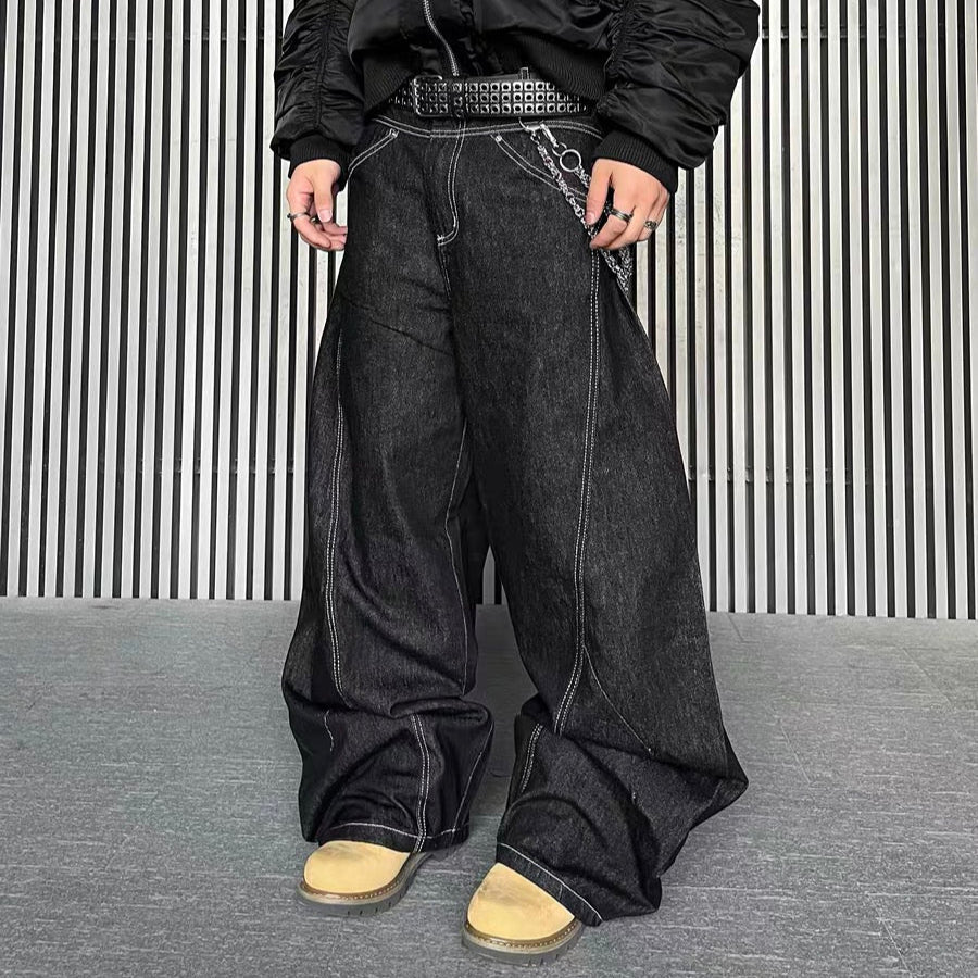Person wearing black wide-leg jeans with white contrast stitching, paired with a black bomber jacket and tan shoes