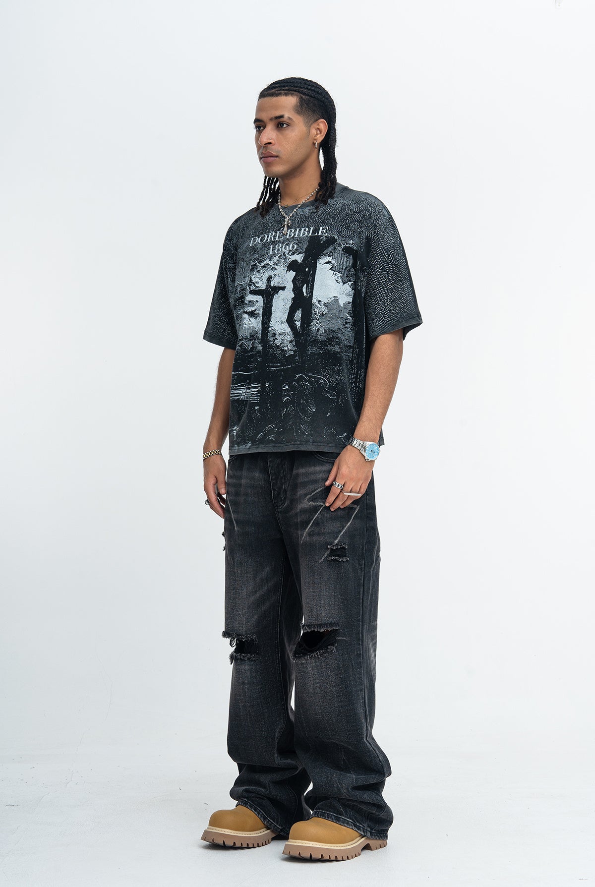 Model wearing a vintage washed black graphic tee with Doré Bible 1866 crucifixion print, paired with distressed jeans and tan boots