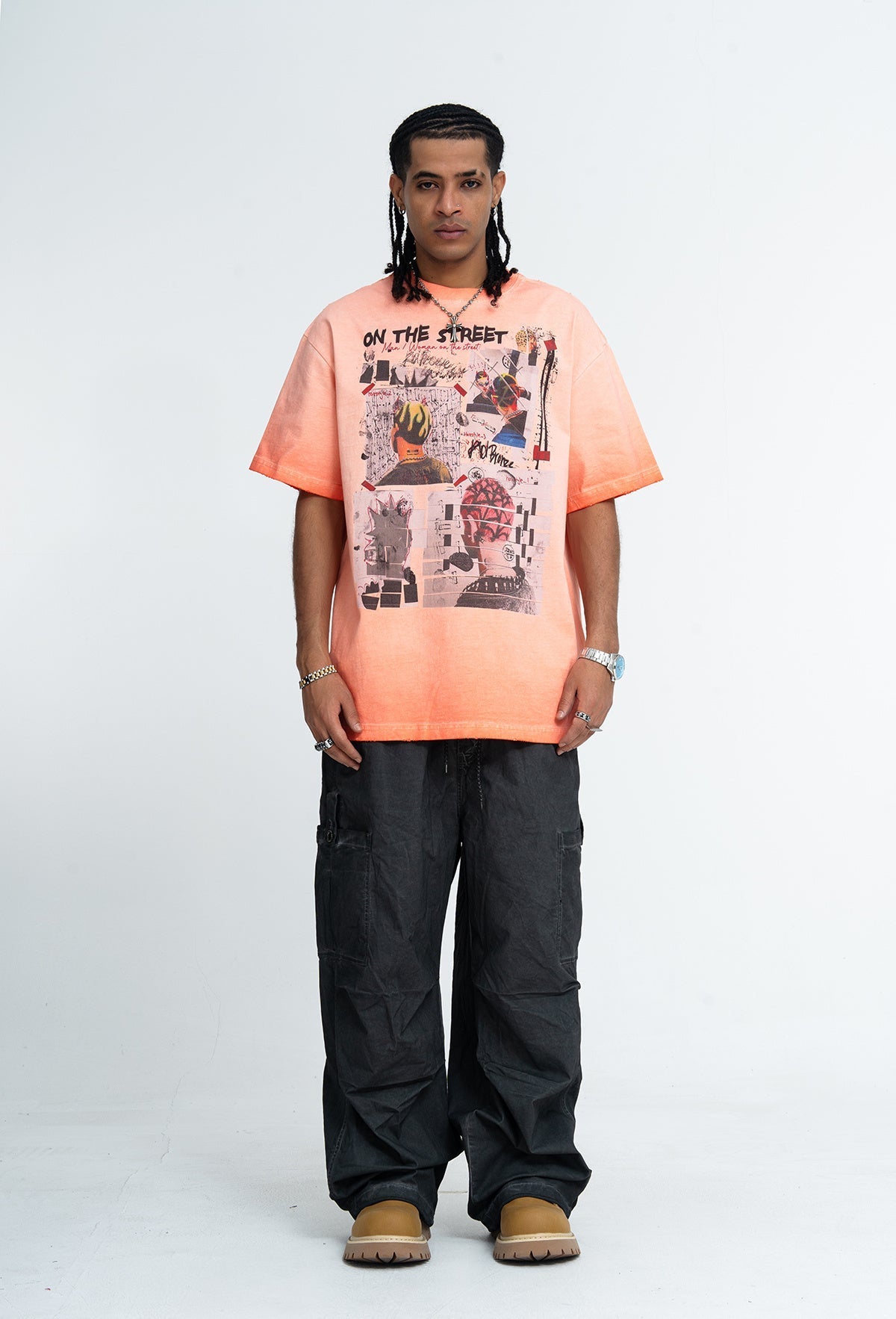Model wearing a peach vintage wash graphic tee with collage street art print, black cargo pants, and tan boots