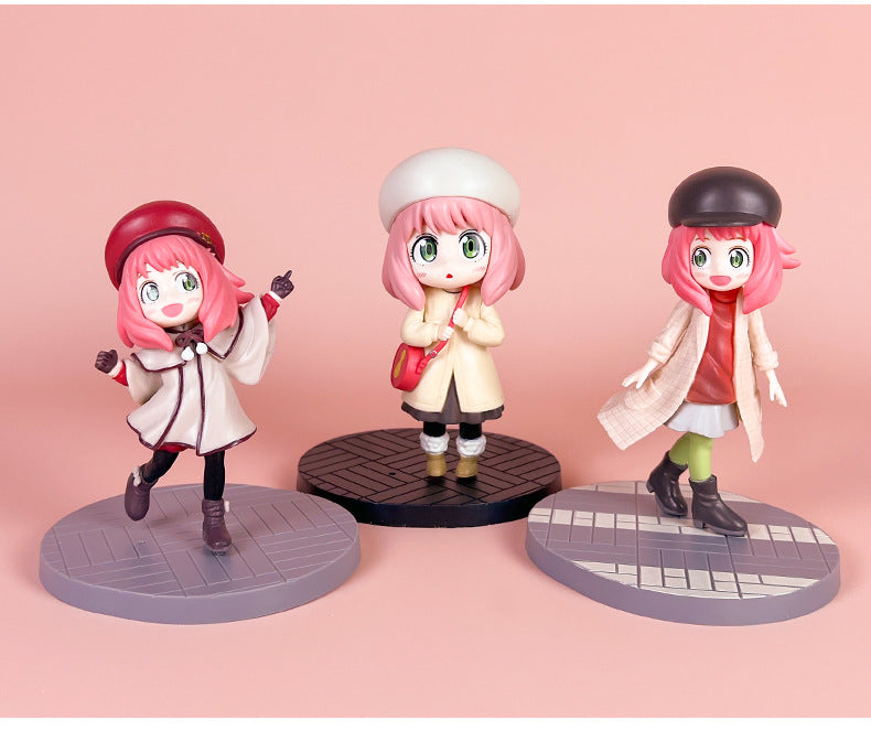 Three figurines of a character with pink hair and green eyes, each wearing a different outfit. They stand on round bases with a pink background.