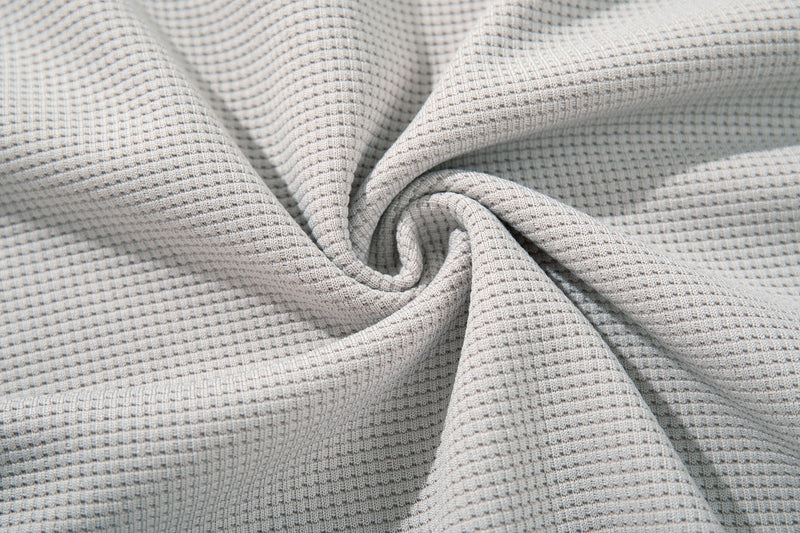 Close-up of light gray waffle-knit fabric with soft folded texture and detailed weave pattern