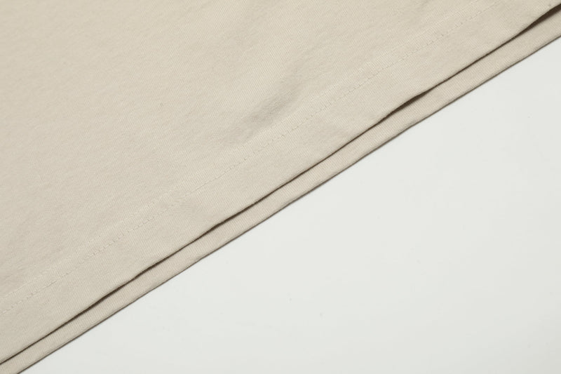 Close-up of beige washed cotton tee hem with folded edge and visible stitching on a clean white background