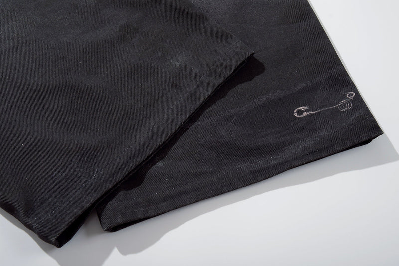 Close-up of lower leg hem on black denim pants with small printed graphic near the cuff