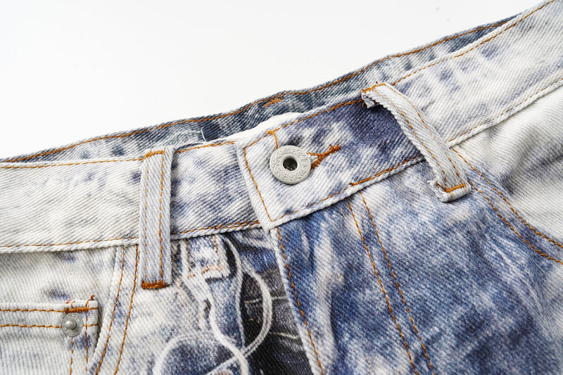 Close-up of the front waistband on faded patchwork denim with button closure and orange stitching