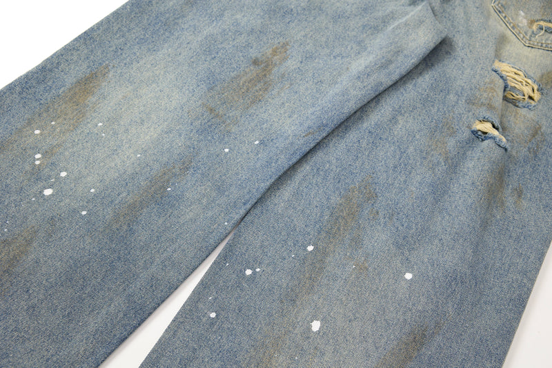 Close-up of faded denim legs with paint-splatter detail and small rips