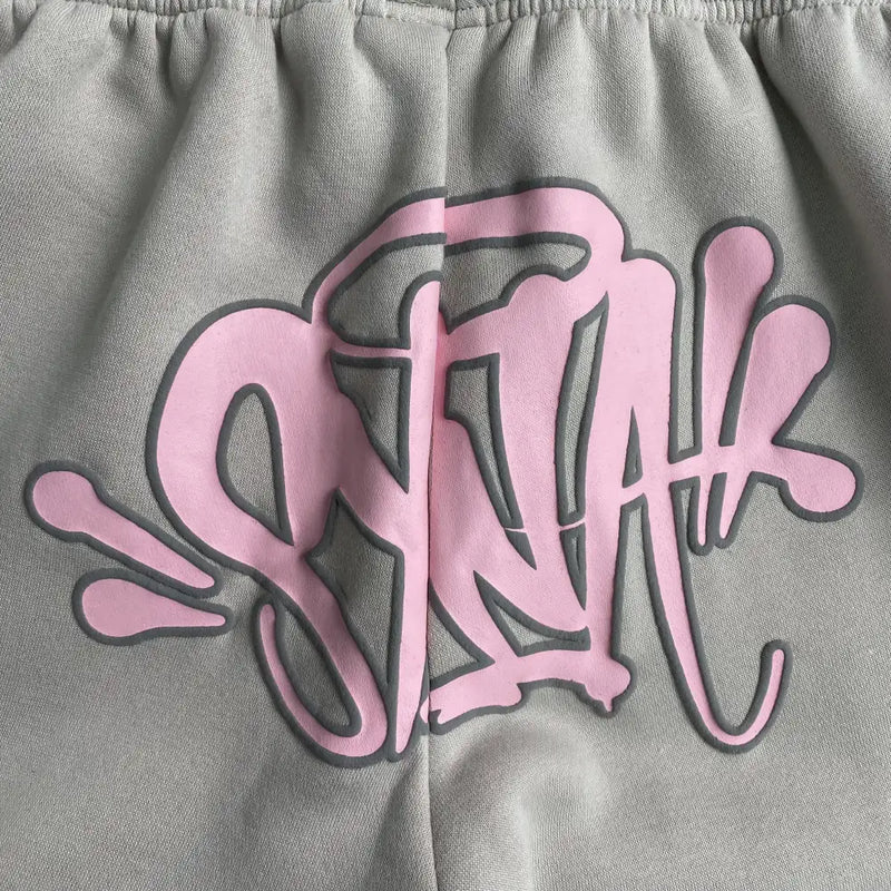 Close-up of gray fabric with stylized pink graffiti text and black outline, echoing Syna World’s bold streetwear vibe—an ideal match for the Syna World Cream Joggers with Pink Drawstring.