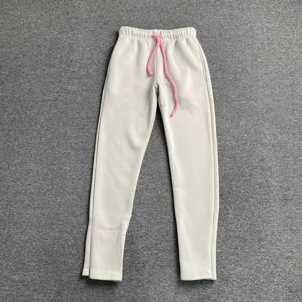 Cream Syna World joggers laid flat, showing pink rope drawstring waistband and script logo embroidery on lower leg