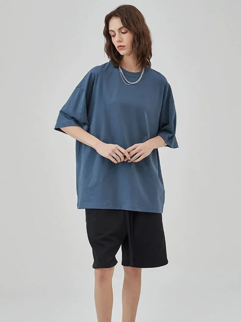 A person wearing a Custom Anime Character Steel Blue T-Shirt - Personalized 230GSM 100% Cotton Tee, paired with black knee-length shorts and a silver chain necklace, stands against a plain light gray background.