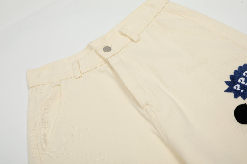 Close-up of cream pants waistband with belt loops, snap button, and stitched seam