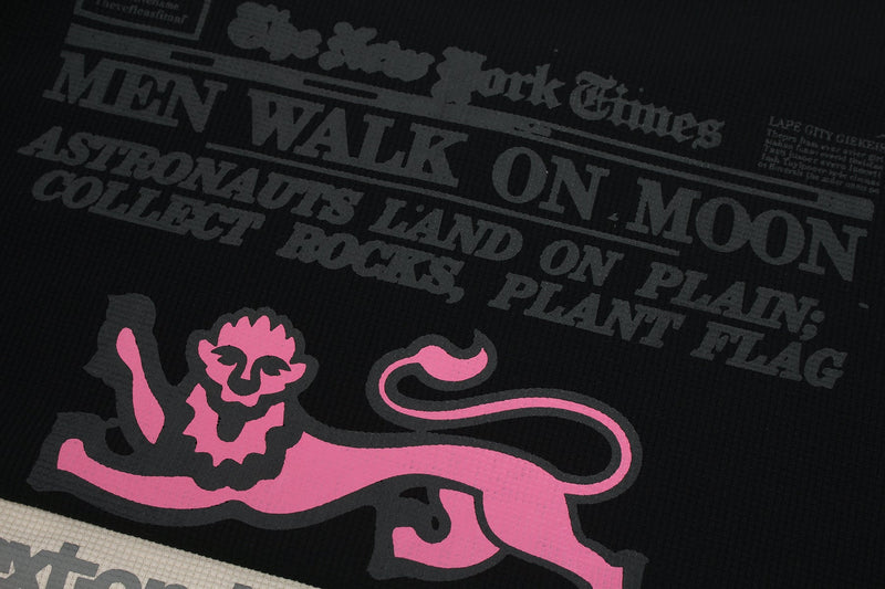 Black waffle tee with a pink leaping lion graphic and faded newspaper-style text print for a retro streetwear look