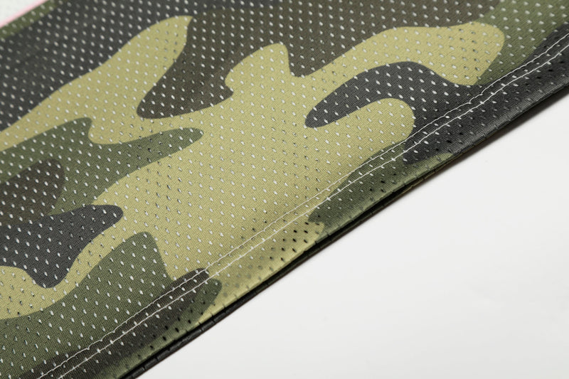 Close-up of olive camouflage mesh jersey fabric with stitched hem and breathable perforations on a white background