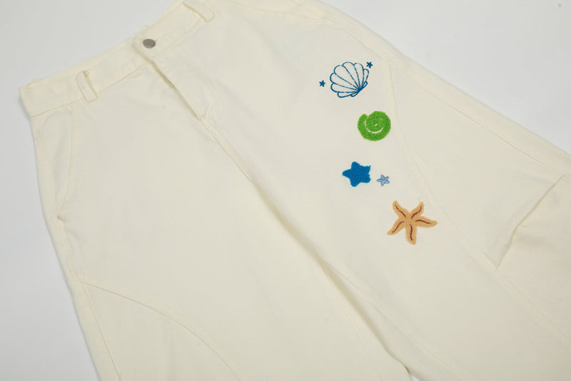Close-up of cream cargo pants front with shell, star, and starfish embroidery