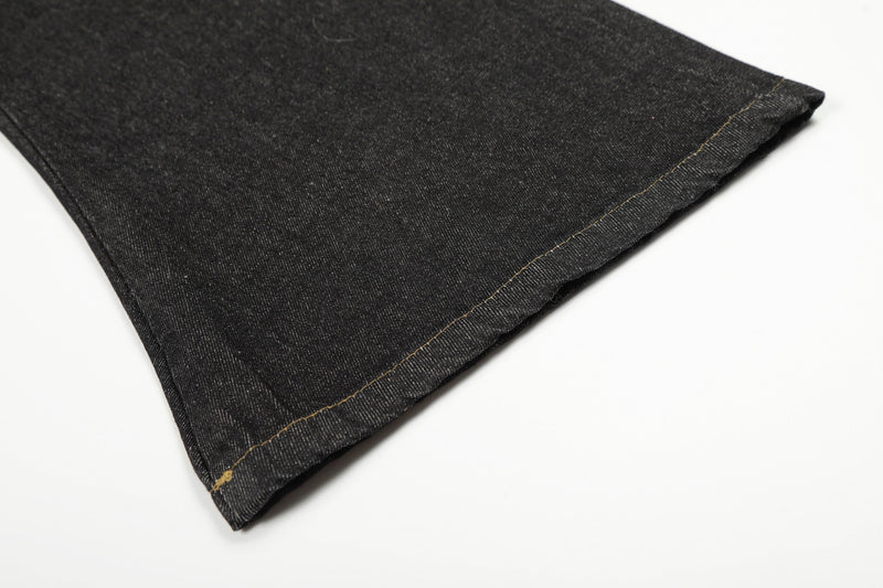 Close-up of a black denim pant leg hem with tan stitching